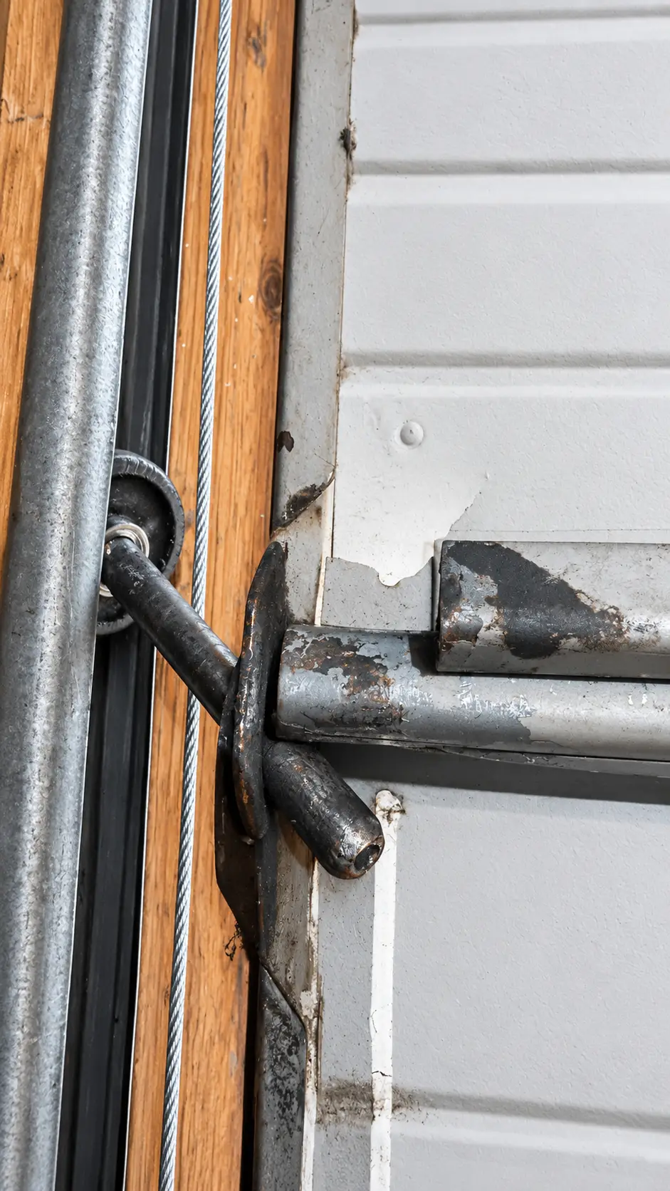Close-up of a creased garage door panel beside its hinge and roller fixture